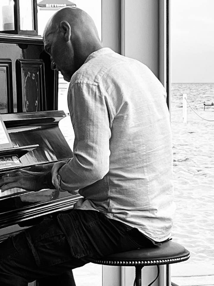 Emanuele Rodighiero al pianoforte verticale sulla spiaggia del Chiosco Faro, Jesolo, con il mare sullo sfondo